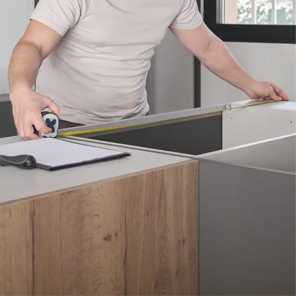 Mann misst einen Küchenschrank mit Maßband, Arbeitsplatte und Fenster im Hintergrund einer modernen Küche